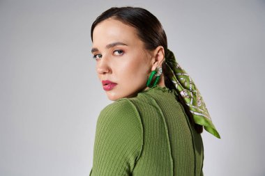 Yeşil moda giyinmiş güzel bir kadının portresi. Gri omuzlara bakıyor.