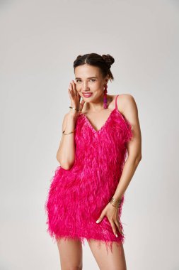 Pembe elbiseli genç esmer kadın kıkırdıyor, gri arka planda yüzüne dokunuyor.