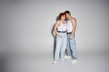 appealing sexy couple in blue jeans posing together lovingly on gray background, relationship clipart
