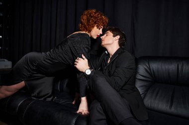 Zarif giysiler içinde çekici erkek ve kız arkadaş siyah koltukta sevgiyle sarılıyorlar, seksi çift.