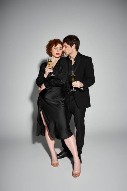 Siyah elbiseli güzel bir kadın. Gri arka planda yakışıklı erkek arkadaşına sarılıyor. Şampanya ellerinde.