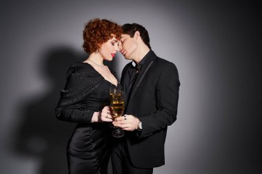 Siyah elbiseli çekici bir kadın. Gri arka planda yakışıklı erkek arkadaşına sarılıyor. Şampanya ellerinde.