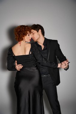 Gri arka planda öpüşen ve kucaklaşan siyah şık elbiseli güzel seksi çift.
