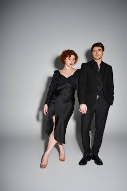 Siyah takım elbiseli çekici bir adam çekici sevgilisinin yanındaki kameraya bakıyor, seksi bir çift.