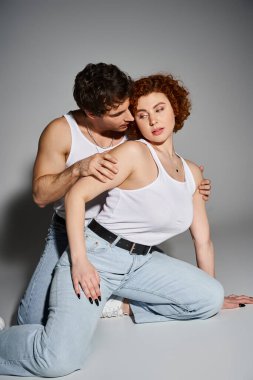 Kot pantolonlu çekici bir adam ve kadın yerde birlikte oturup sıcak, seksi bir çift gibi sarılıyorlar.