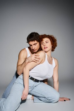 appealing man and woman in blue jeans sitting on floor together and hugging warmly, sexy couple clipart