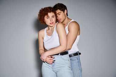 Kotlu yakışıklı bir adam kameraya bakarken güzel kız arkadaşına sarılıyor, seksi bir çift.