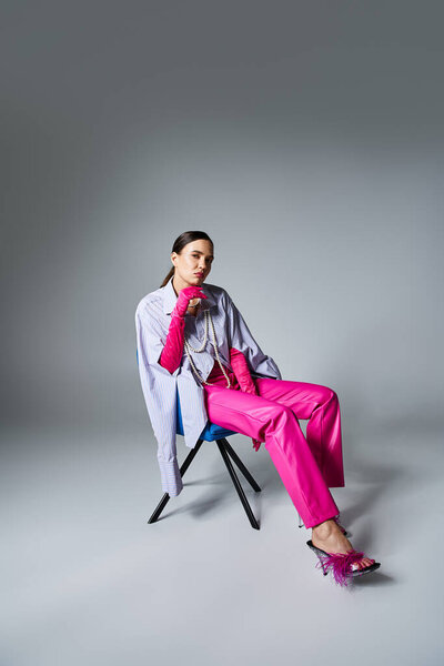 Уверенная брюнетка в стильном наряде и шикарных перчатках трогает ее лицо, сидит на стуле