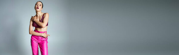 Brunette woman in pink trousers and dark red top, wearing stylish jewelry, hands on her body, banner