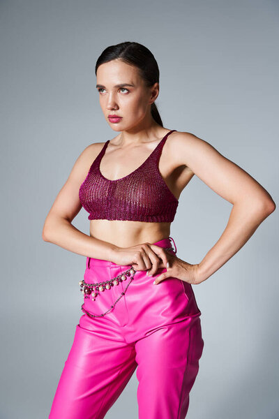 Chic brunette girl in stylish knitted bordeaux top touching thigh, looking away on grey background