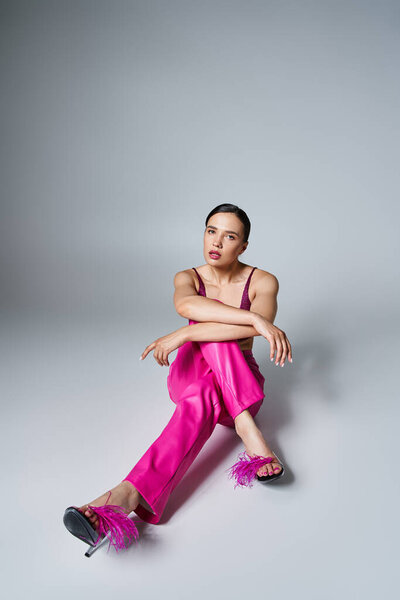 Confident brunette woman in trendy red top and pink pants and shoes, sitting crossing her legs