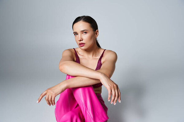Pretty brunette woman wearing knitted bordeaux top and pink pants, sitting with crossed hands
