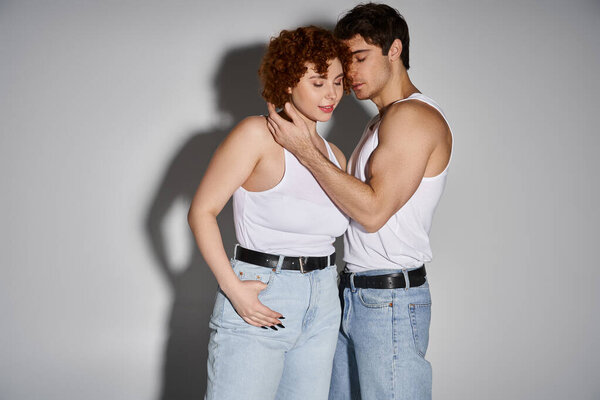 appealing sexy couple in blue jeans posing together lovingly on gray background, relationship