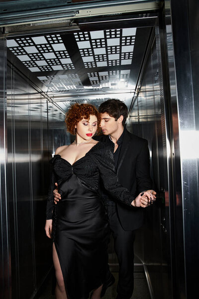 sexy alluring couple in elegant black dress and suit hugging lovingly in elevator after date
