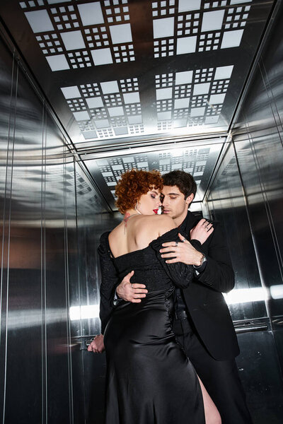 сексуальная красивая пара в элегантном черном платье и костюме, обнимающаяся с любовью в лифте после свидания