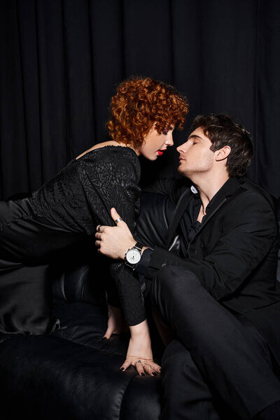 соблазнительный парень и девушка в элегантной одежде обнимаясь с любовью на черном диване, сексуальная пара
