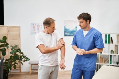 Mavi üniformalı yakışıklı doktor randevusu sırasında olgun hastasını dinliyor.