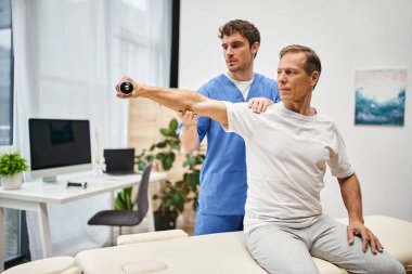 Mavi cüppeli yakışıklı doktor, rehabilitasyondaki halterli yakışıklı hastasına yardım ediyor.