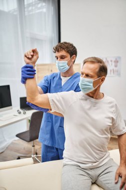 Maskeli ve eldivenli çalışkan doktor yetişkin hastaların koğuşta kaslarını iyileştirmesine yardım ediyor.