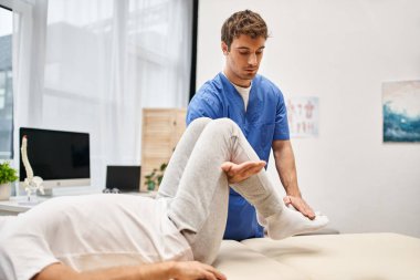 Tıbbi üniformalı çekici bir doktor, yetişkin hastasının koğuşta kaslarını iyileştirmesine yardım ediyor.