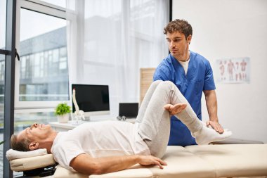 Mavi cüppeli yakışıklı doktor, yakışıklı, olgun hastasına vücudunu iyileştirmesi için yardım ediyor.