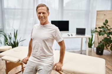 Çekici, olgun bir hasta hastane koğuşunda poz veriyor ve rehabilitasyonda kameraya gülümsüyor.