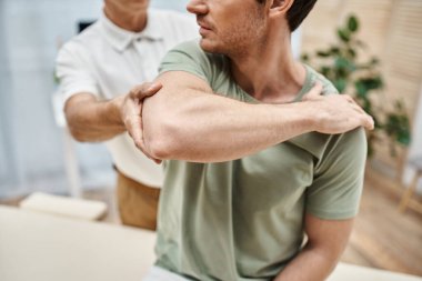 cropped view of mature doctor in uniform helping his patient to stretch during rehabilitation clipart