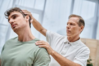 İyi görünümlü olgun bir doktor hastasının dizlerini kontrol ediyor, rehabilitasyon konsepti.