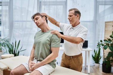İyi görünümlü olgun bir doktor hastasının dizlerini kontrol ediyor, rehabilitasyon konsepti.