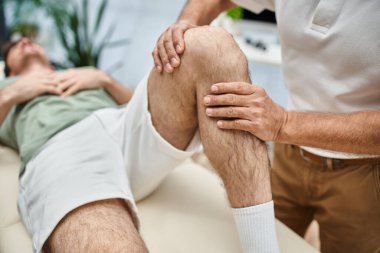 İyi görünümlü olgun bir doktor hastasının dizlerini kontrol ediyor, rehabilitasyon konsepti.