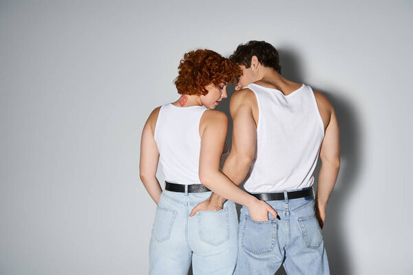 back view of loving man and woman in blue casual jeans posing together on gray backdrop, sexy couple