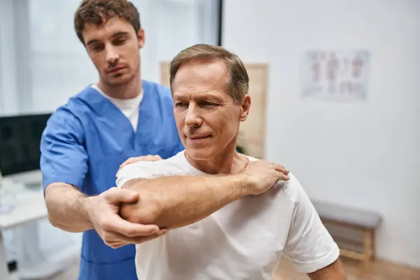穿着休闲装的成熟男人在医生的帮助下伸展肌肉 — 图库照片