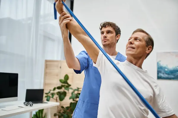 Handsome Doctor Helping Mature Merry Attractive Patient Use Resistance Band — Stock Photo, Image