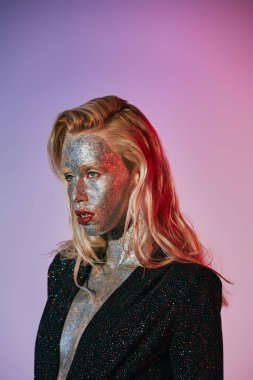 Parlak makyajlı, parlak elbiseli, pembe gradyan üzerinde poz veren etkileyici sarışın kadın portresi.