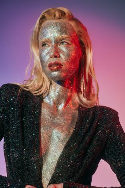 Parlak makyajlı ve parlak elbiseli güzel bir kadının portresi pembe arka planda poz veriyor.