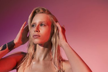 Pembe arka planda dövmeli, şık kırmızı elbiseli çekici bir kadın model.