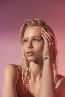 Kırmızı elbiseli güzel bir bayan model pembe arka plana bakıyor.