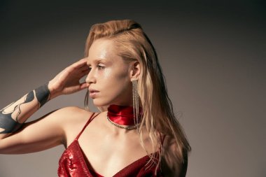 Aksesuarları ve dövmeleri olan çekici genç bir kadın model. Gri arka planda poz veriyor ve başka yöne bakıyor.