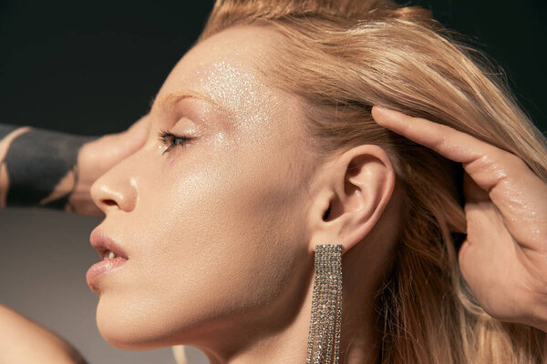 портрет стильной молодой женщины с татуировкой и подсветкой, собирающей волосы и отводящей взгляд