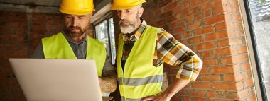 good looking construction workers in safety vests working with laptop, cottage builders, banner clipart