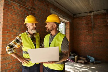 hardworking construction workers in safety vests working with laptop on site, cottage builders clipart