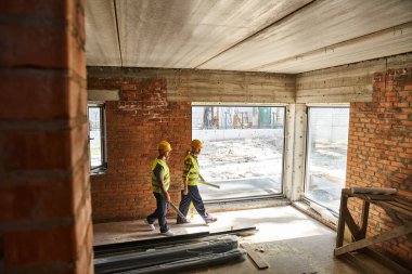 Güvenlik yelekleri içindeki iki çalışkan adam bina planlarıyla ve katıyla birlikte çalışıyor, kulübe inşaatçıları.