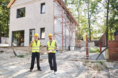 Bina planlarıyla ve iskelenin yanında kameraya bakarak poz veren yakışıklı yazlık sahipleri.