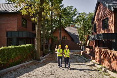 good looking construction workers in safety helmets walking and discussing site, cottage builders clipart