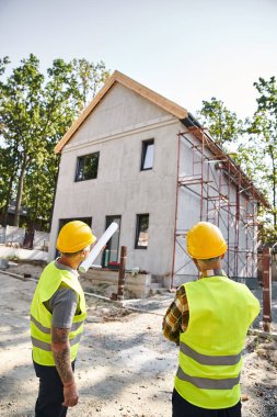 Güvenlik miğferleri takmış özverili kır evi inşaatçılarının arka plan manzarası.