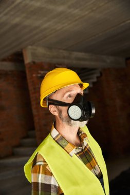 Güvenlik kaskı ve yeleği olan, toz maskeli, inşaat alanında çalışan güzel görünümlü bir kulübe inşaatçısı.
