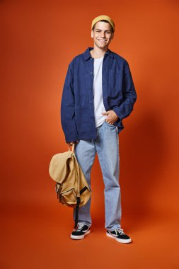 happy student in casual outfit with grey eyes and backpack posing on terracotta background clipart