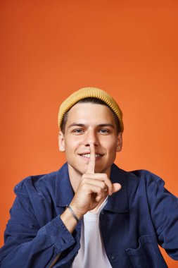 portrait of smiling man in his 20s showing sign of silence against terracotta background clipart