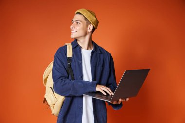 Sırt çantasıyla dizüstü bilgisayara bağlanan gülümseyen öğrenci ve terracotta arka planına karşı taraf arıyor