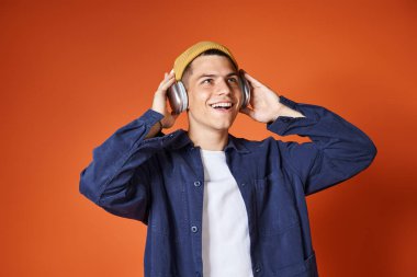 charming young man in yellow listening to music with headphones on terracotta background clipart